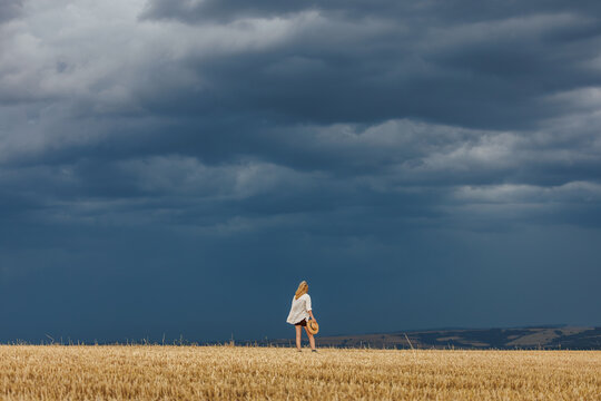 Female farmer watching dark storm clouds over harvested agricultural field. Extreme weather caused by climate change