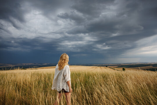 Woman farmer looking at coming storm clouds over agricultural field. Rainstorm arrival, environmental issues in farming