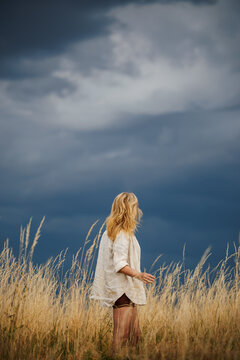 Woman standing in dry grass and looking at approaching storm clouds on horizon. Summer weather