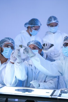 Microchip engineers hold a silicon wafer up for inspection in a high-technology cleanroom while wearing white lab coats and blue protective gloves and modern scientific (No. 4434).
