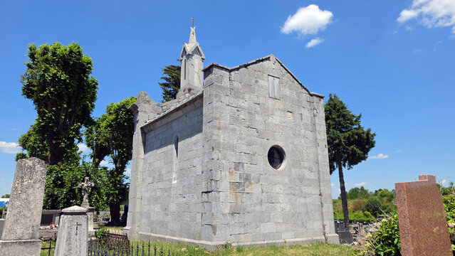Grey ashlar stone mausoleum chapel with a small belfry tower in a sunny cemetery