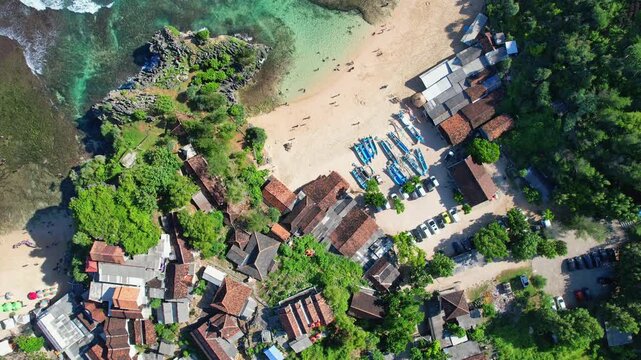 Aerial drone footage from above of Ngandong beach in Gunungkidul regency, Yogyakarta, Java island, Indonesia, with white sand, cristal turquoise water, reef, fishing boats and restaurants