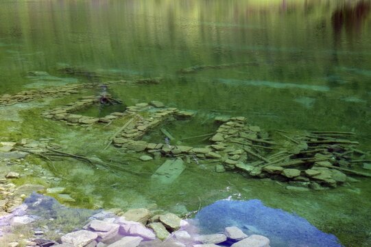 Clear, green water with visible stones and ruins underneath, surrounded by natural landscape, foundation walls of a sunken village, N&ouml;rangsdalen, Norway