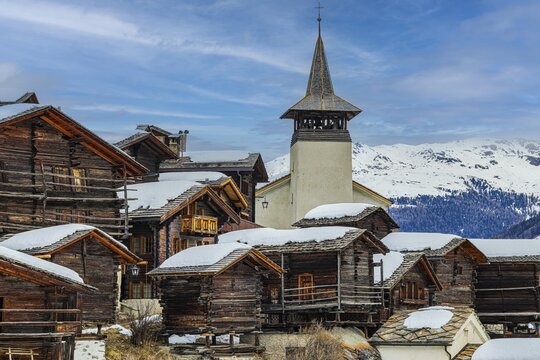 Old wooden houses with snow-covered roofs and the Saint Theodule church in the historic village centre, Grimentz, Val d'Anniviers, Valais Alps, Canton Valais, Switzerland
