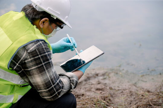 Ecologist examines water quality with digital tablet alongside a calm water body focusing on environmental monitoring and research
