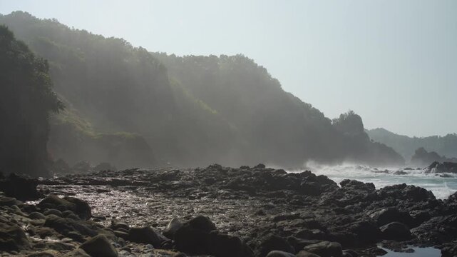 Misty Rocky Coastline with Waves Breaking over Dark Coastal Rocks, Dramatic Sea Cliffs, and Ocean Spray, Creating a Moody Atmospheric Seascape with Rugged Natural Texture