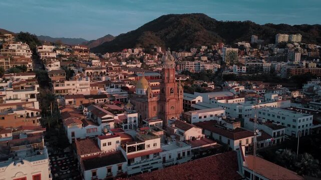 Drone orbital sunset footage of Parroquia Nuestra Senora de Guadalupe church showcasing architectural tower against warm magenta light with coastal city backdrop