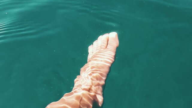 V&iacute;deo grabado en primera persona con un pie en primer plano sobre el mar, rodeado de agua turquesa y movimiento suave de la superficie. La escena transmite descanso, verano, libertad y relajaci&oacute;n en u