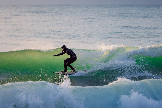 Surfer male riding on glassy wave in ocean with evening sunlight