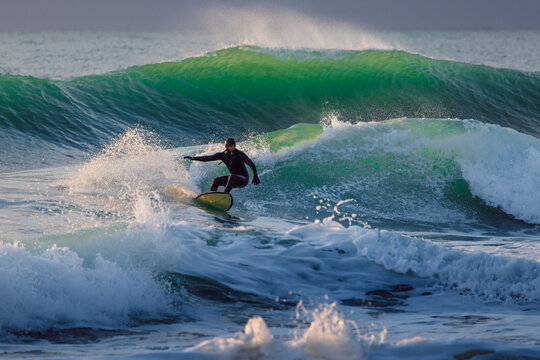 Surfer on wave in cold ocean. Winter surfing with evening sunlight