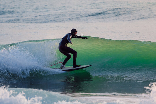 Surfer man rides on glassy wave in winter ocean with evening sun light