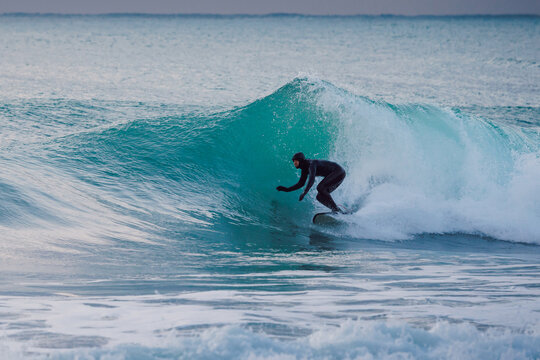 Surfer rides on wave in ocean. Winter cold surfing on waves