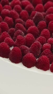 Vertical video. Close-up of fresh raspberries covering a round wedding cake with white frosting.