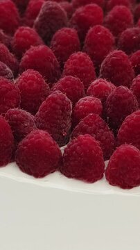 Vertical video. Macro view of ripe raspberries on a round wedding cake with smooth white frosting.
