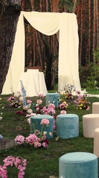Vertical video. Wedding cake beside a ceremony arch in a pine forest during an outdoor wedding.