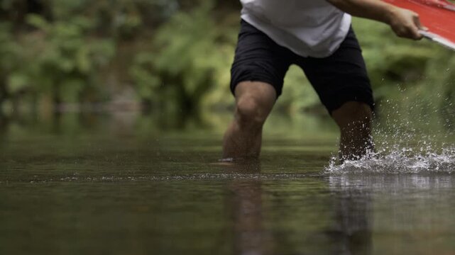 Man swinging board across shallow river water surface - Low, slow motion shot
