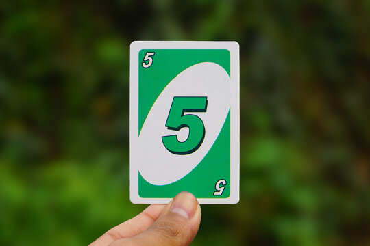 Hand Holding Green Number 5 UNO Card Against Blurred Background 