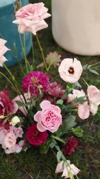 Vertical video. Close-up of pink wedding flowers arranged on grass beside the ceremony seating area.