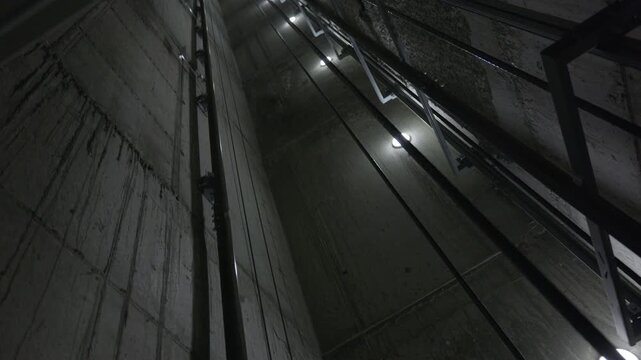Looking up inside elevator shaft with guide rails and maintenance lighting