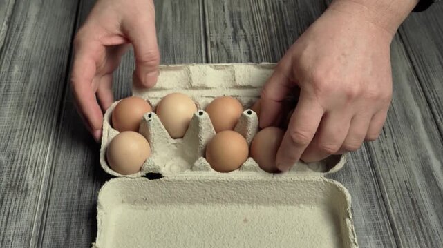 Hands take eggs from a cardboard box on a wooden surface, emphasizing organized preparation for a breakfast fire