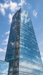 Fototapeta premium Low angle view of a modern glass skyscraper reflecting the blue sky and white clouds