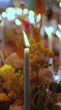 Vertical video. Burning candle surrounded by wedding flowers on a banquet table with bokeh lights.