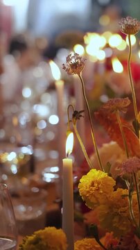 Vertical video. Close-up of a lit candle with floral decor on an elegant wedding reception table.