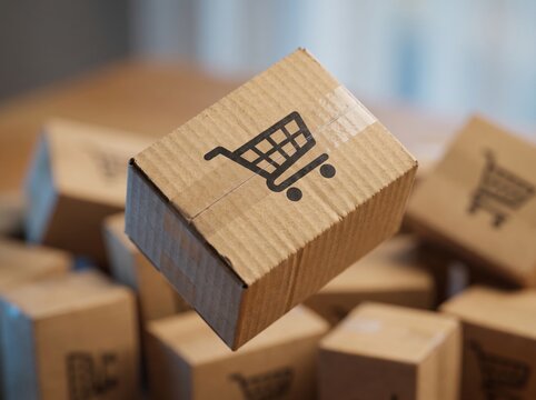 Cardboard parcel box mid-air with shopping cart icon on pile of boxes, online shopping