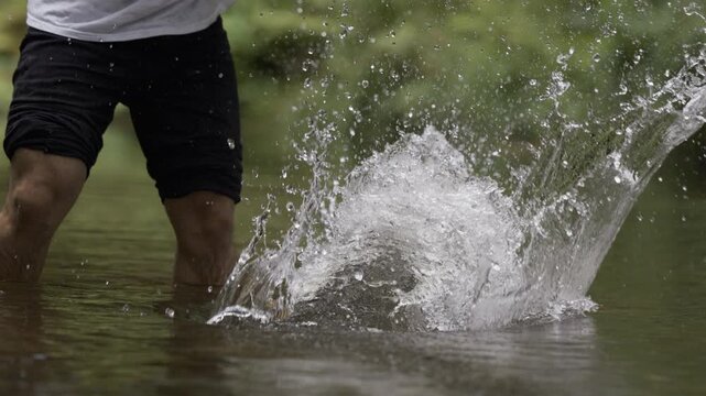Low, Slow Motion Shot Of Man Using Large Board To Make Splashes In Shallow River