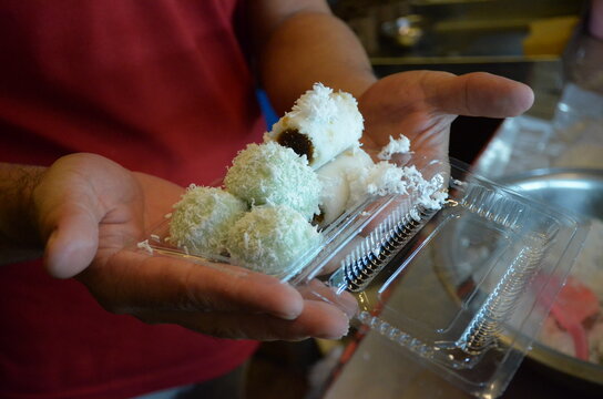 Traditional Indonesian coconut cake putu dessert served in a plastic takeaway box, a photo of a handmade sweet treat with authentic street food appeal.