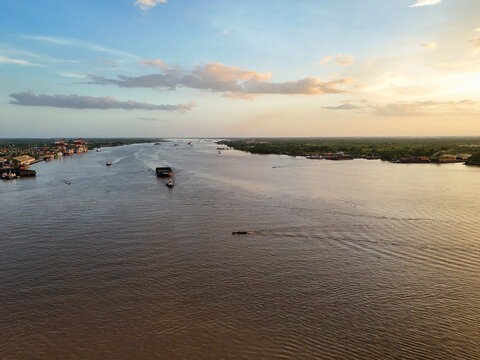 Aerial view of Barito River with cargo barges and small boats navigating the waterway at sunset in Banjarmasin, South Kalimantan, Indonesia.