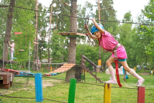 A cheerful girl goes through obstacles while holding on to the rope of a suspended rope course