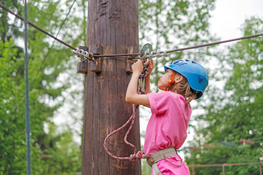 Close-up of a child wearing a blue sports helmet attaching a carabiner to a safety rope