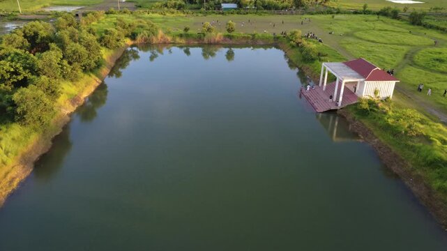 Aerial view of rural pond and sports field with people relaxing at sunset in a green countryside landscape