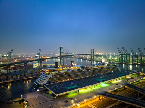 Aerial view of the Long Beach Cruise Center with a cruise ship docked at the terminal and the Gerald Desmond Bridge in the background in Long Beach, California, United States.