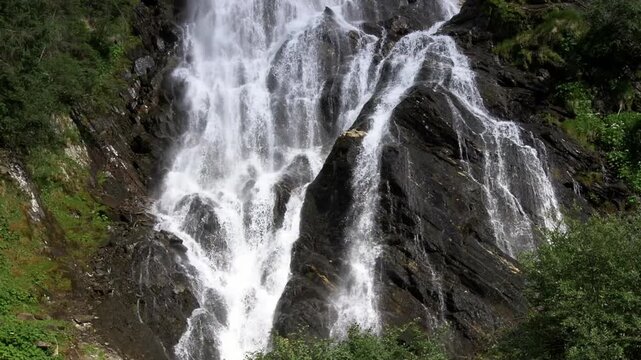 Powerful mountain waterfall cascading down a massive black stone cliff