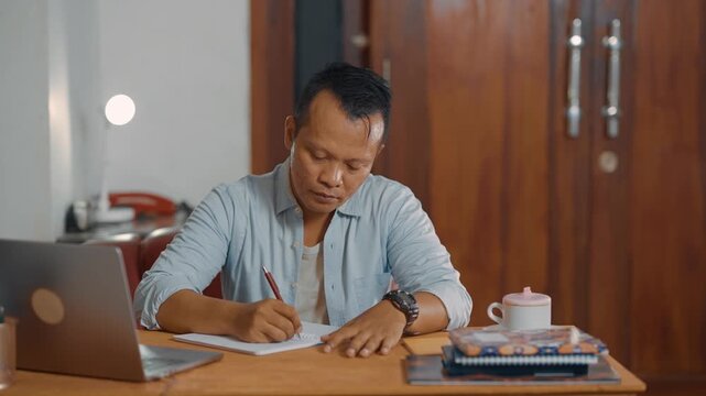 Student adult Asian man using laptop and writing on notebook. Learning, exam and education concept.