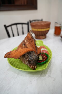 Crispy whole fried fish served with spicy sambal and fresh vegetables on a green plate, authentic Indonesian cuisine, perfect for restaurant, culinary, and travel photography.