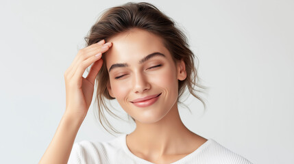 Fototapeta premium Attractive young woman with closed eyes touching forehead with hand and broadly smiling on a white background with free space