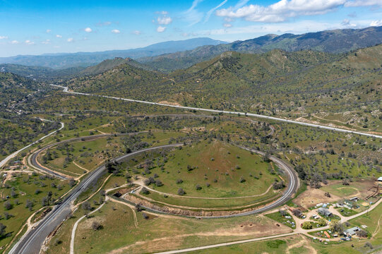 Aerial view of the Tehachapi Railroad Loop winding around a green hill in a mountainous landscape, Bear Valley Springs, California, United States.