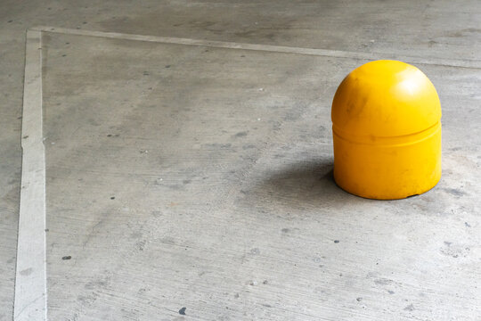 Bright yellow safety bollard and white painted lines on an empty concrete parking garage floor.