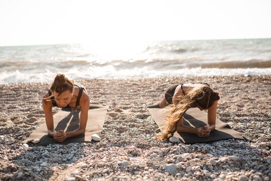 Two teenage girls 15-16 year old doing yoga class standing in plank at beach over sea background in sunny day. Healthy active lifestyle. Teenagerhood. Summer season.