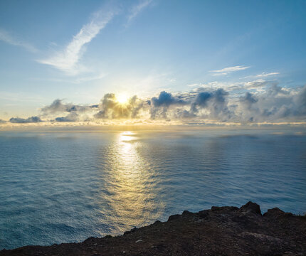 Breathtaking golden sunset over the calm Atlantic ocean with sun rays breaking through clouds at Ponta do Pargo, Madeira, Portugal.