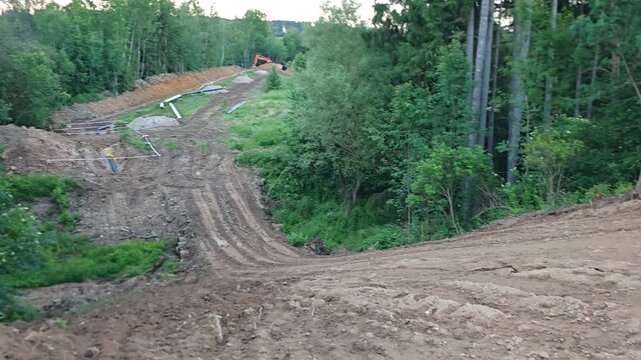 Excavator working on a pipeline construction site cutting through a dense green forest landscape