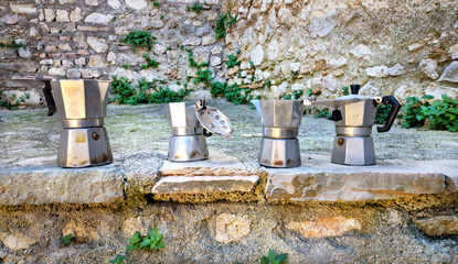 Naklejka premium Vintage moka coffee pots row on medieval stone ledge backdrop. Traditional Italian espresso culture slow travel lifestyle . Roccantica Italy High Resolution. Wal art print decor, old world charm