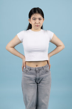Confident young Asian woman standing with hands on hips looking at camera