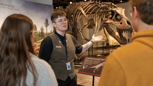 Professional Museum Docent Explaining Tyrannosaurus Rex Skeleton to Visitors at Natural History Exhibit