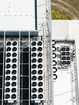Aerial view of multiple industrial HVAC cooling units and ventilation fans arranged in rows on a flat white rooftop in Riga, Latvia.