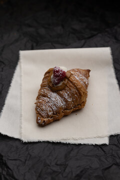 Croissant artesanal relleno con crema, frambuesa y az&uacute;car glass sobre tela de lino con fondo oscuro