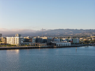 Obraz premium Oakland California waterfront showing urban development with modern residential buildings along the bay, backed by hills under a clear sky